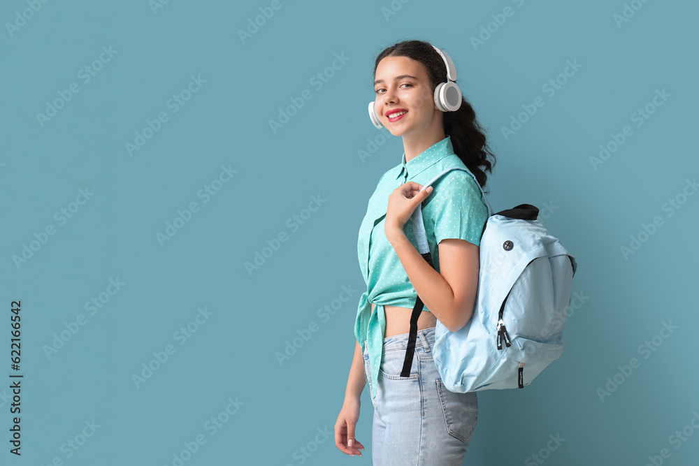 Female student in headphones with backpack on blue background