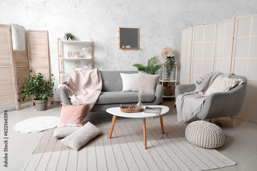 Interior of light living room with cozy grey sofa, armchair and mirror