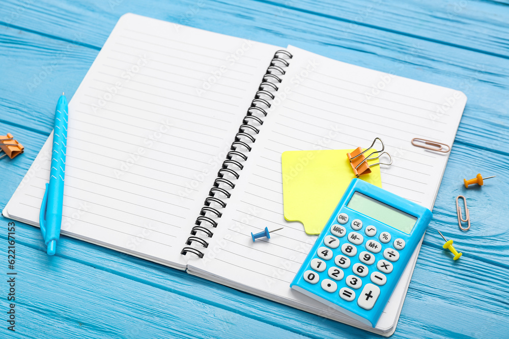 Blank notebook with calculator and stationery on wooden blue background