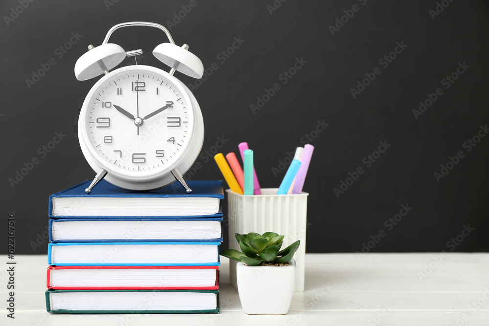 Different stationery with alarm clock on white table against black chalkboard