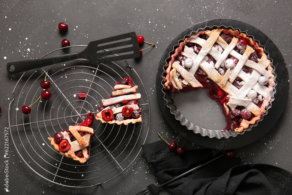 Baking dish with tasty cherry pie and stand of pieces on black background