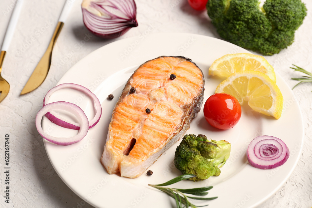 Plate with tasty grilled salmon steak, vegetables and lemon on light background