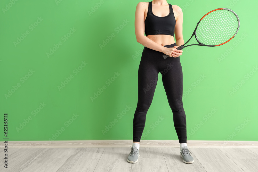 Young woman in sportswear and with tennis racket near green wall