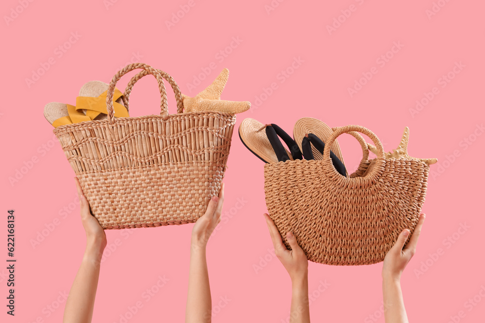 Hands with wicker beach bags and flip-flops on pink background