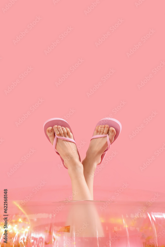 Legs of woman in flip-flops and inflatable ring on pink background