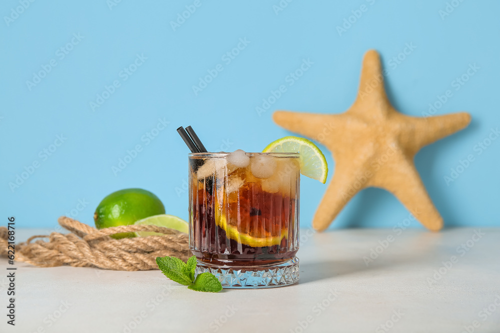 Glass of cold Cuba Libre cocktail and starfish on white table