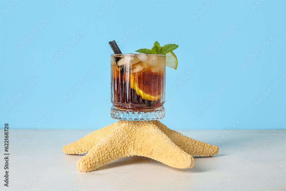 Glass of cold Cuba Libre cocktail and starfish on white table