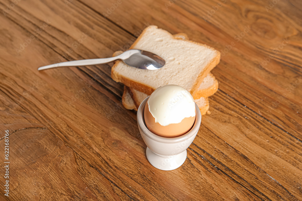 Holder with boiled chicken egg and bread on wooden background