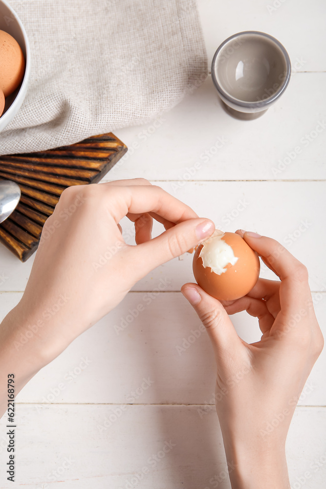 Woman peeling boiled chicken egg on white wooden background