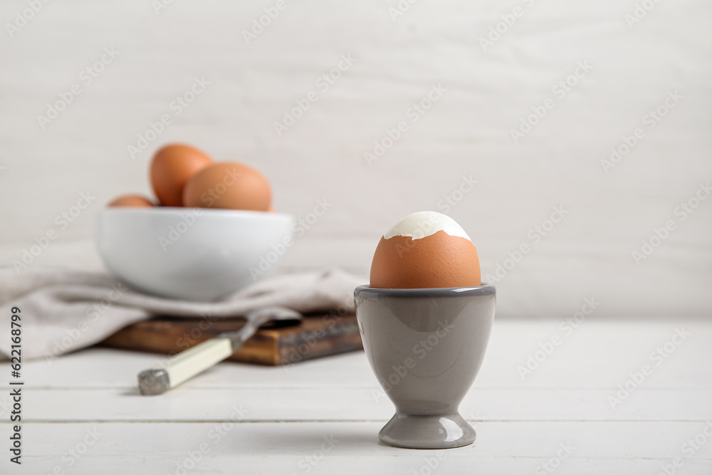 Holder with boiled chicken egg on white wooden background