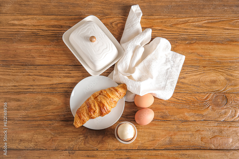 Holder with boiled chicken egg and plate of croissant on wooden background