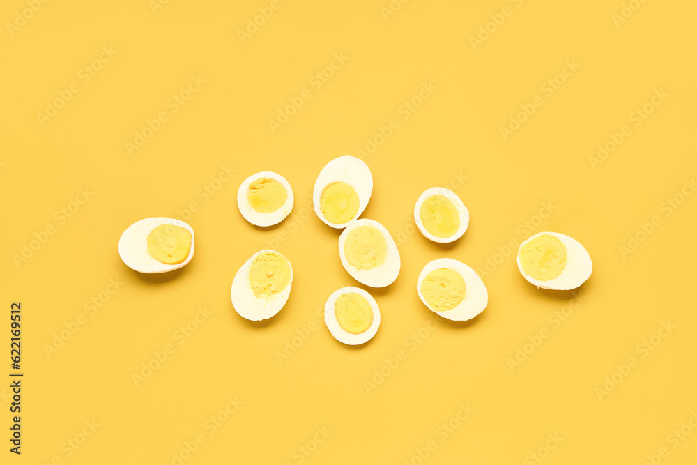 Halves of tasty boiled eggs with slices on yellow background