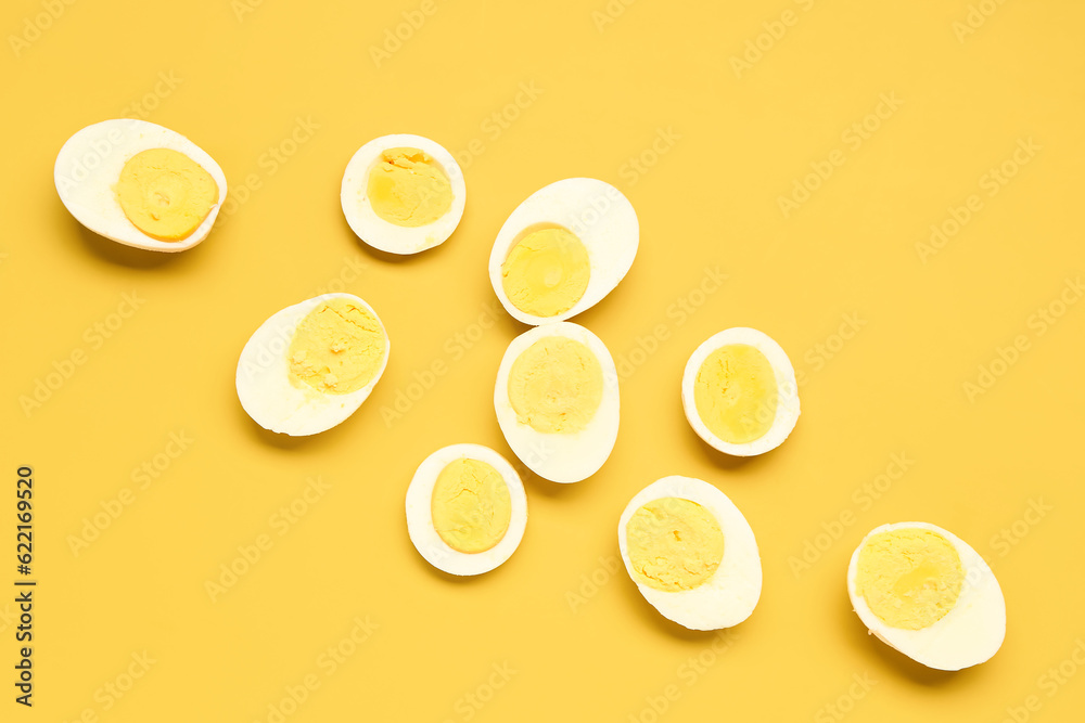 Halves of tasty boiled eggs with slices on yellow background