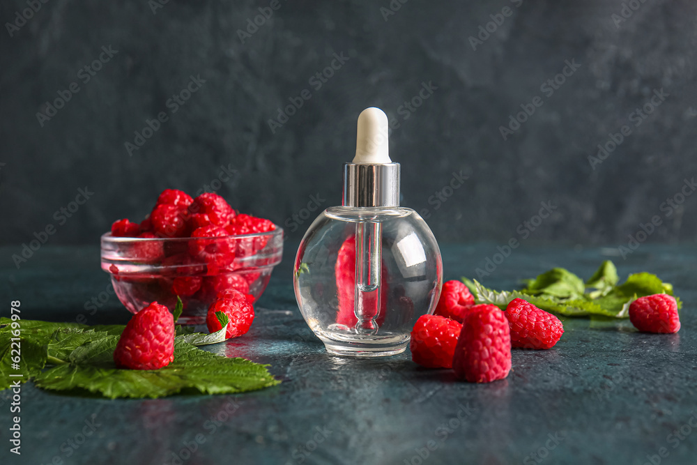 Bottle of cosmetic raspberry oil and bowl with berries on dark background