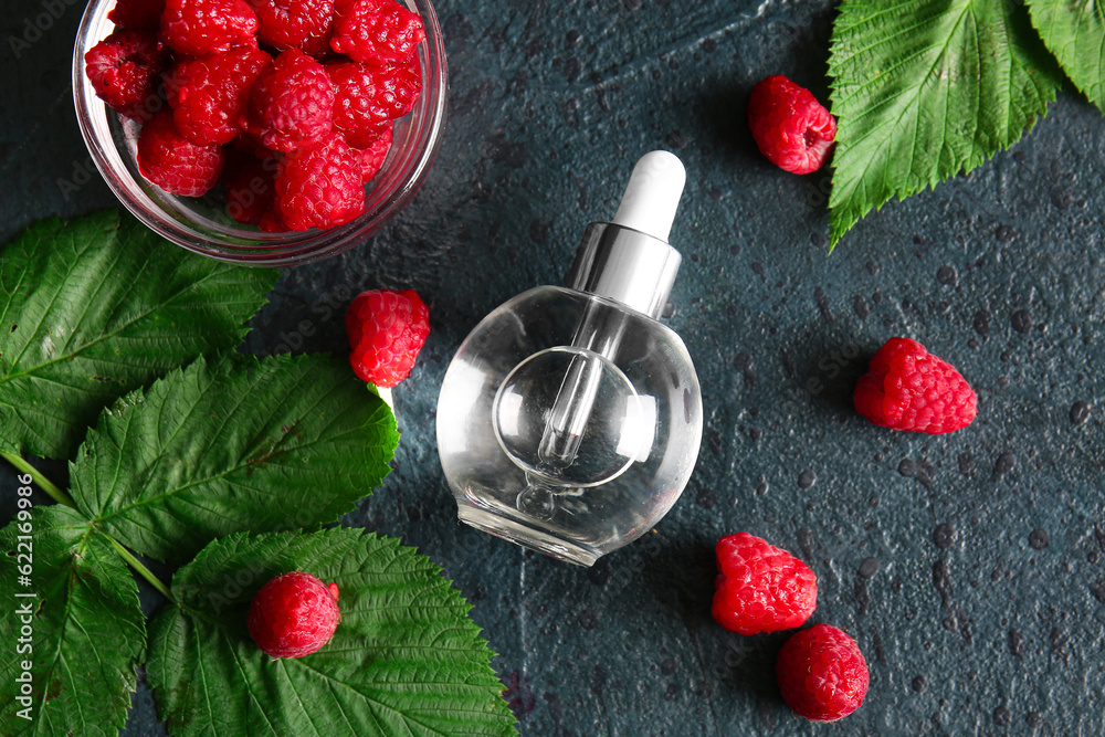 Bottle of cosmetic raspberry oil and bowl with berries on dark background