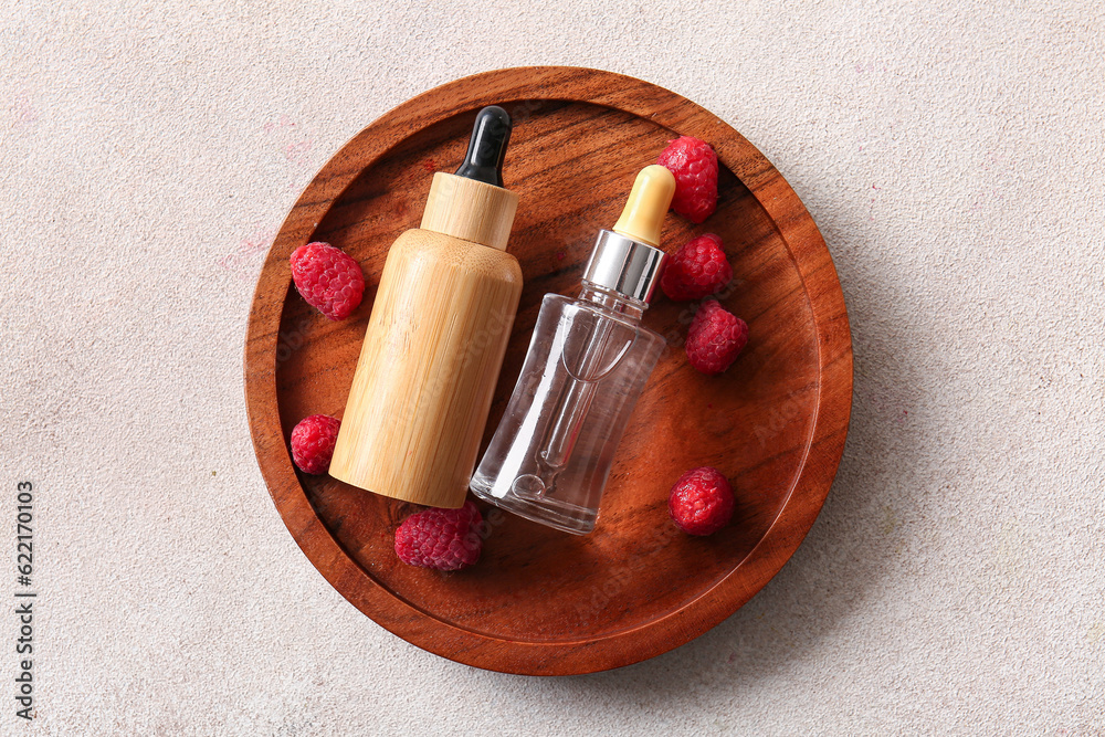 Wooden plate with bottles of cosmetic raspberry oil on white background