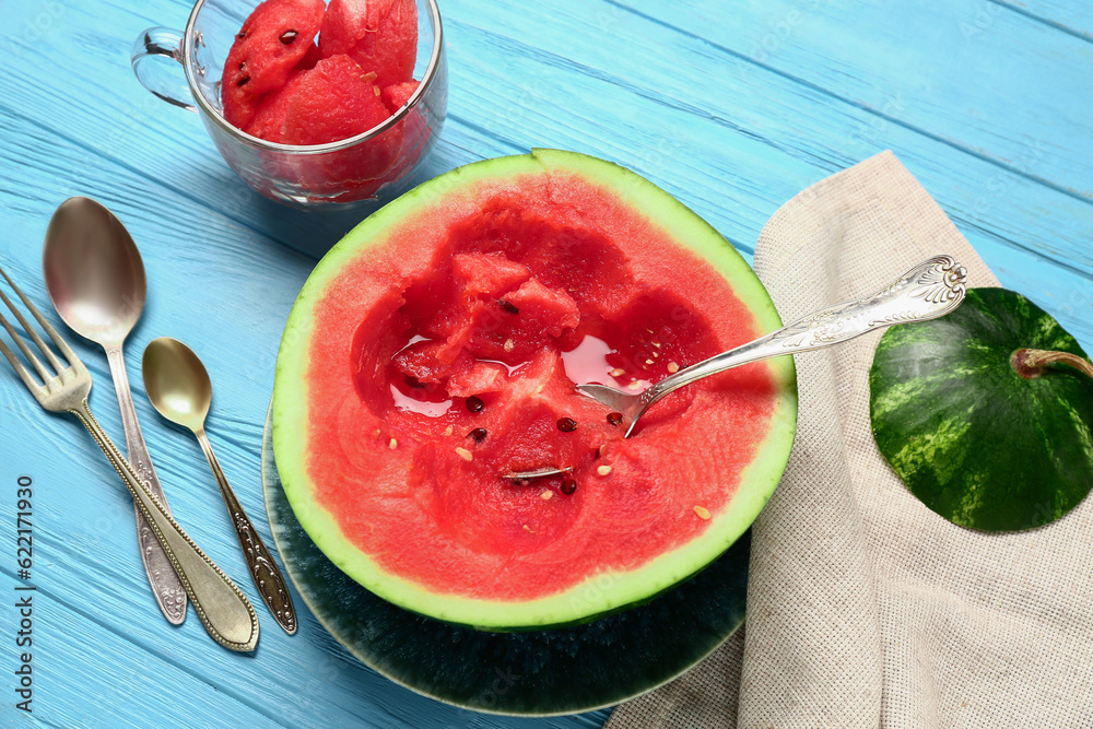 Half of fresh watermelon and cup with pieces on blue wooden background