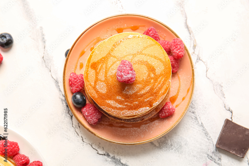 Plate of tasty pancakes with raspberries on white marble background