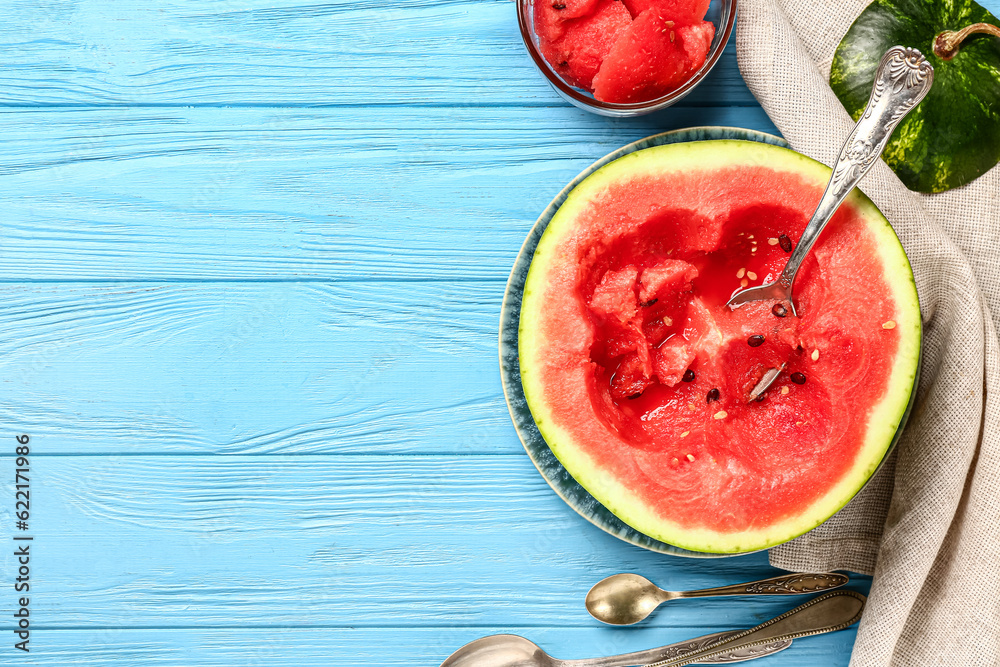 Half of fresh watermelon and cup with pieces on blue wooden background