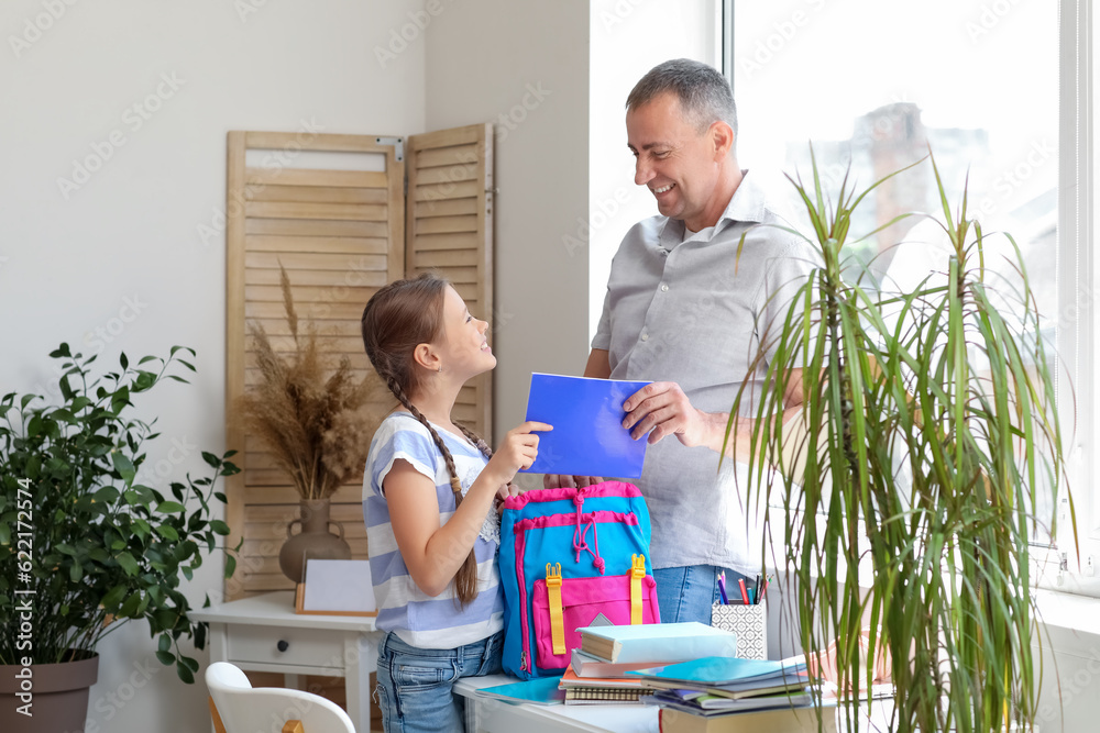 Father helping his little daughter to pack schoolbag at home