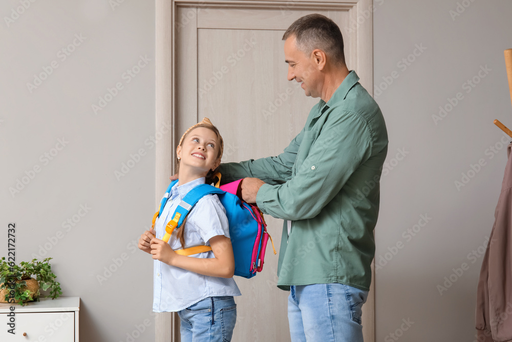 Father helping his little daughter to put schoolbag on in hall