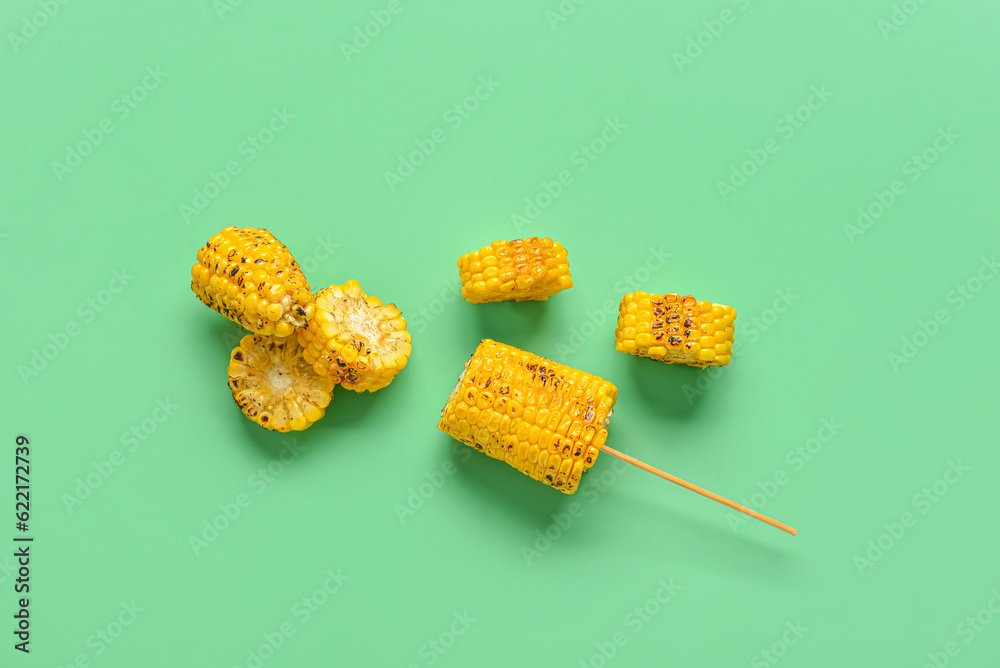 Cut tasty grilled corn cobs on green background