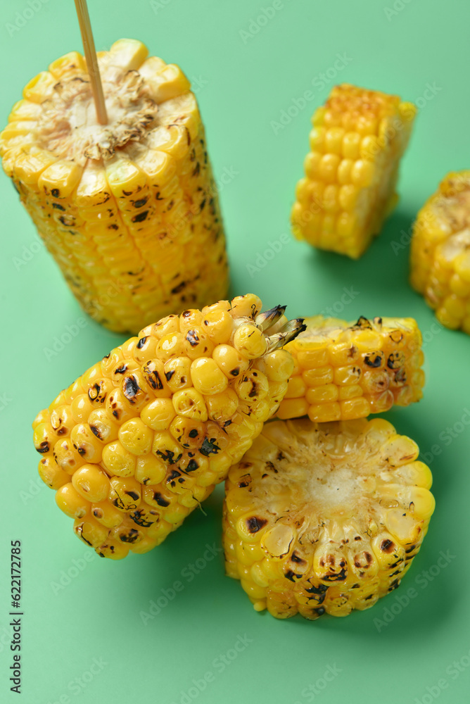 Cut tasty grilled corn cobs on green background