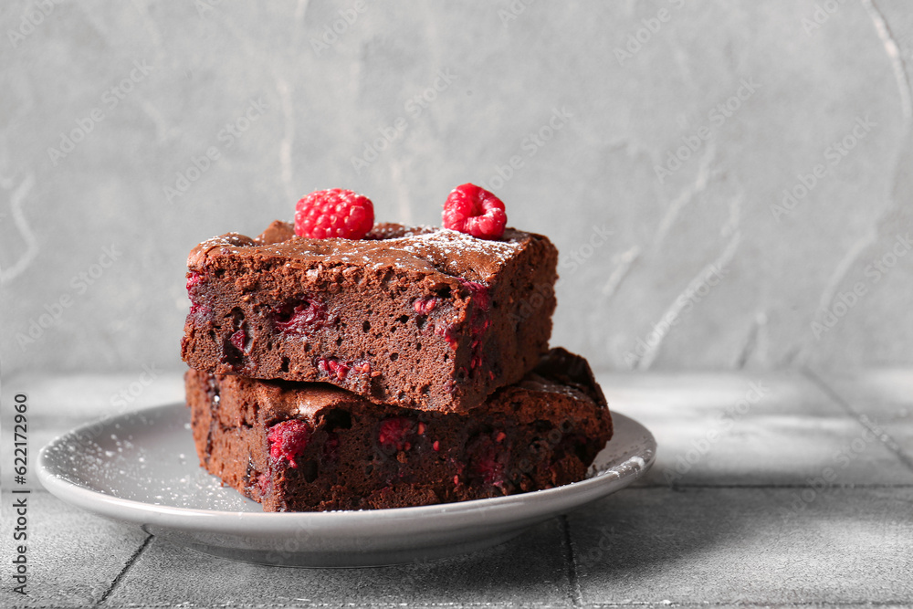 Plate with pieces of raspberry chocolate brownie on grey tile table