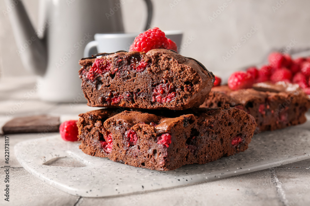 Board with pieces of raspberry chocolate brownie on grey tile table