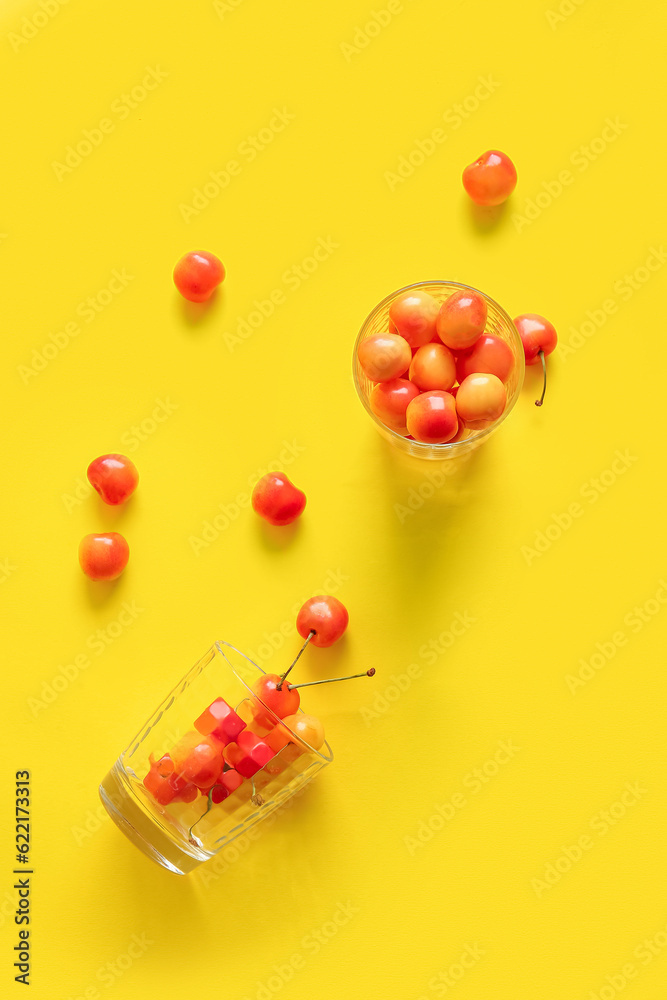 Cups with sweet yellow cherries on yellow background