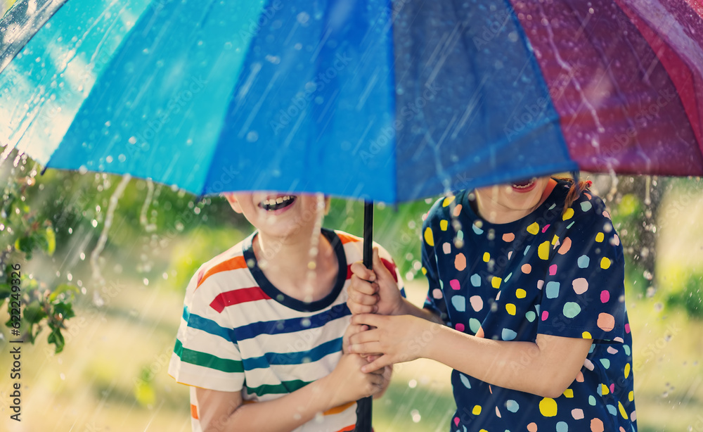 Boy and girl standing outdoors in rainy day under colourful umbrella.