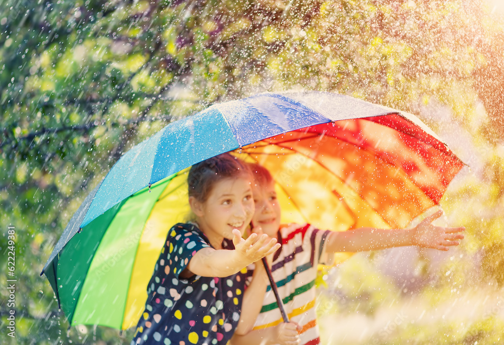 Boy and girl standing outdoors in rainy day under colourful umbrella and trying to catch any raindro