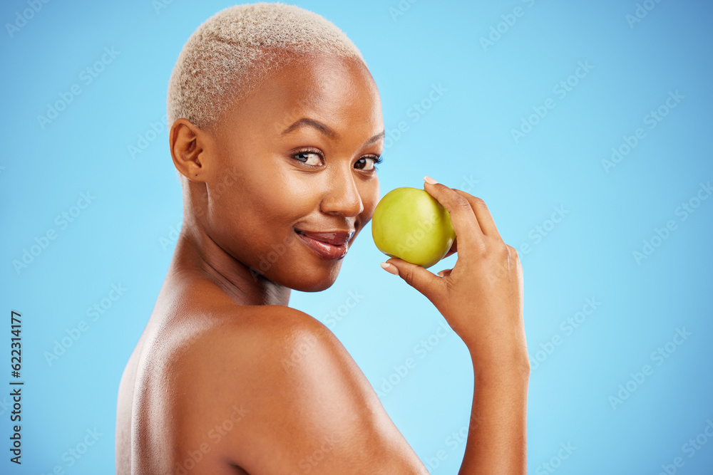 Happy black woman, portrait and apple for nutrition or healthy diet against a blue studio background