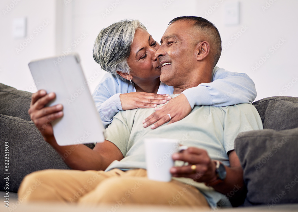 Senior couple, hug and tablet on sofa to relax with quality time in home with kiss during retirement