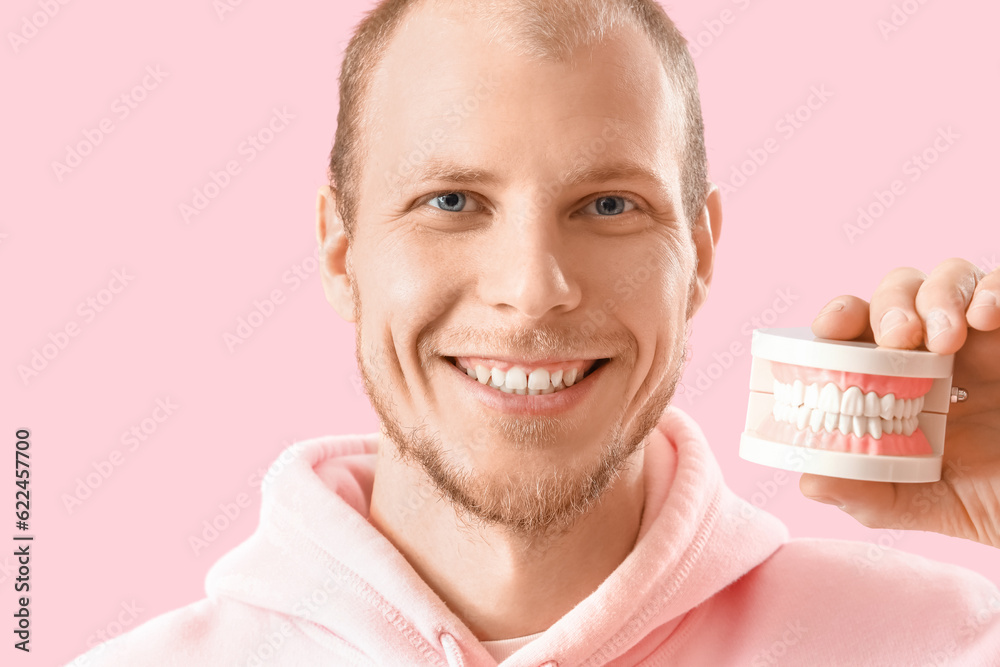 Young bearded man with jaw model on pink background, closeup