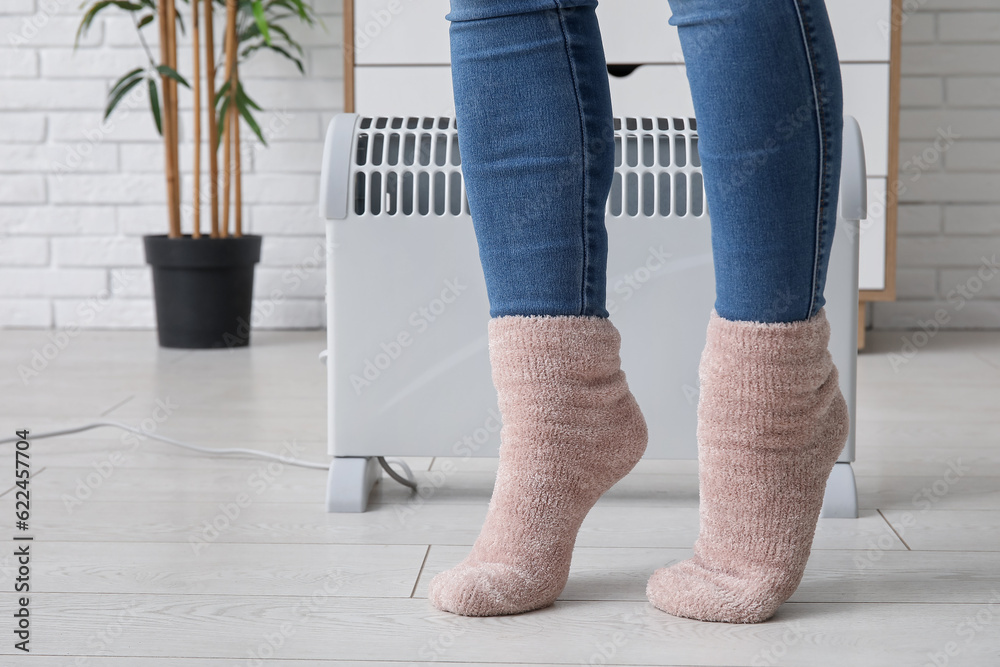 Woman in warm socks near radiator at home, closeup