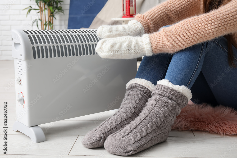 Woman warming hands in mittens near radiator at home, closeup