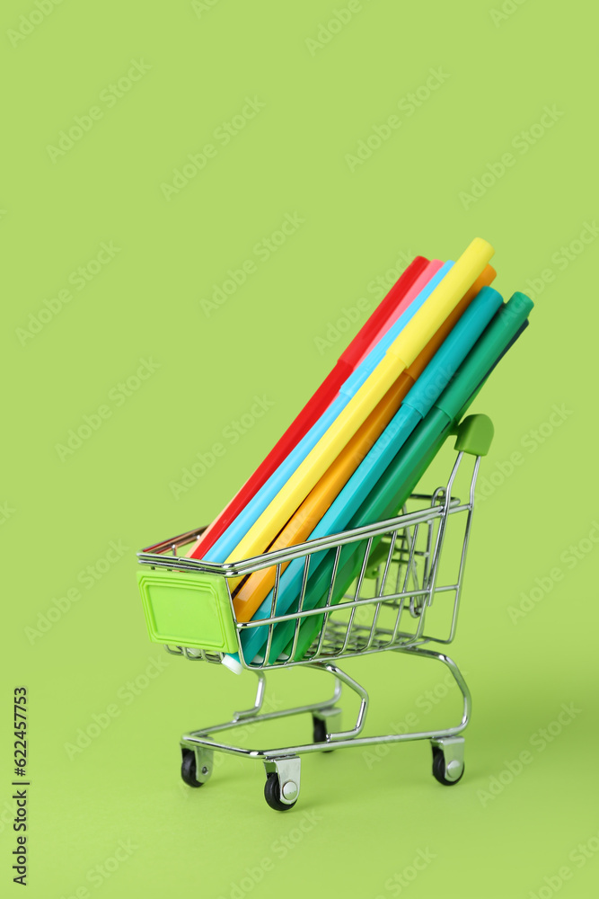 Shopping cart with pencils on green background