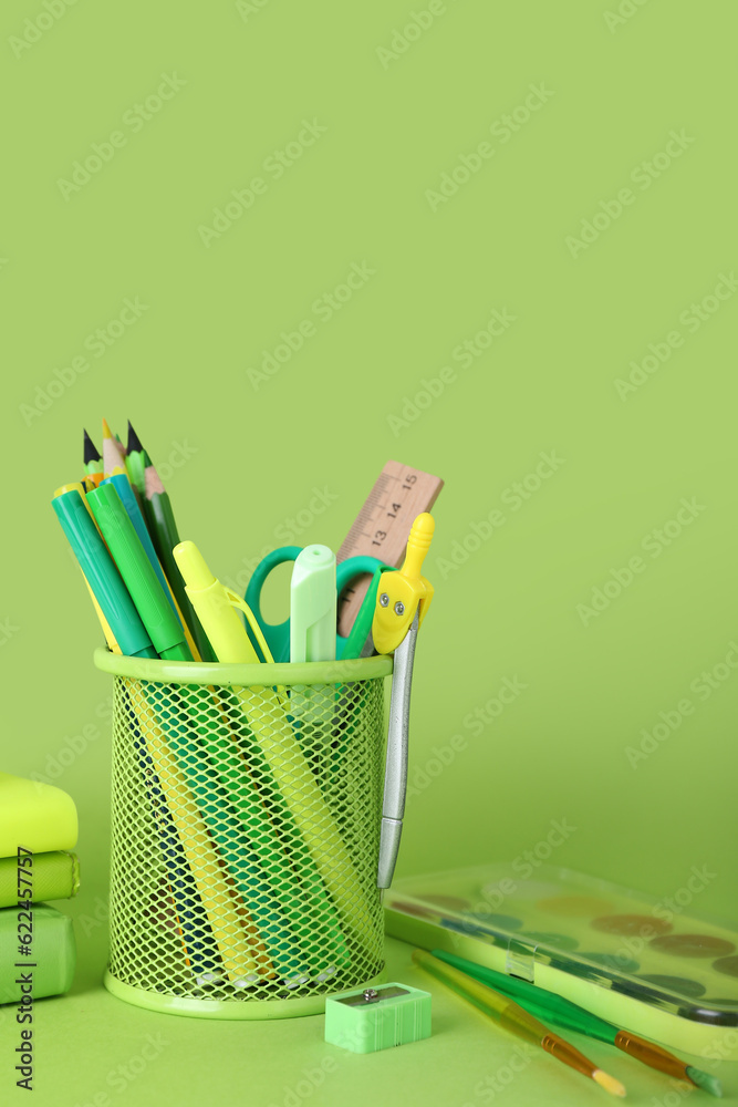 Holder with stationery, paint and brushes on green background