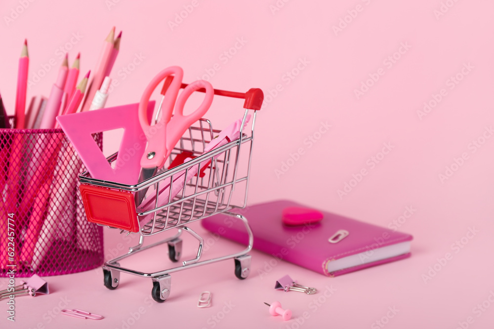 Shopping cart with stationery on pink background