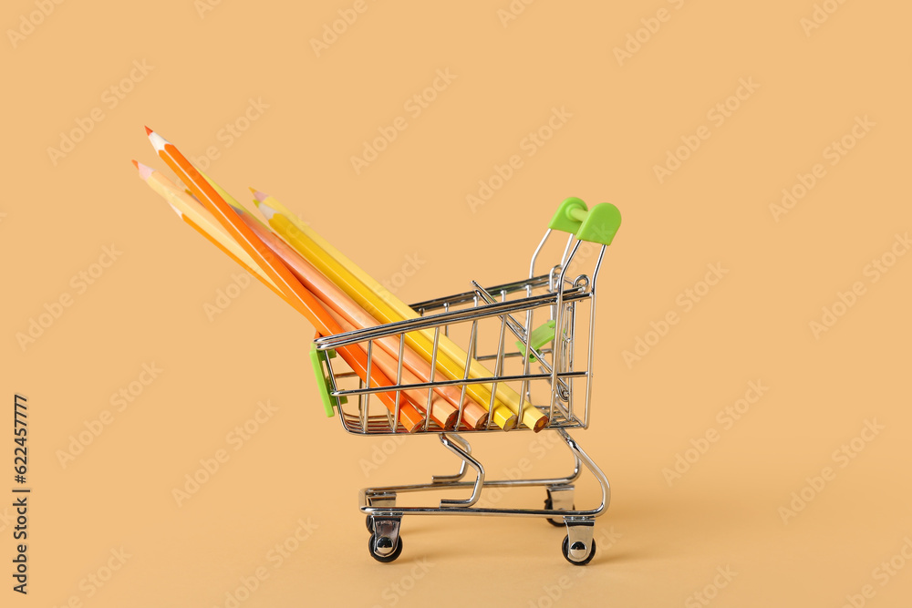 Shopping cart with pencils on color background