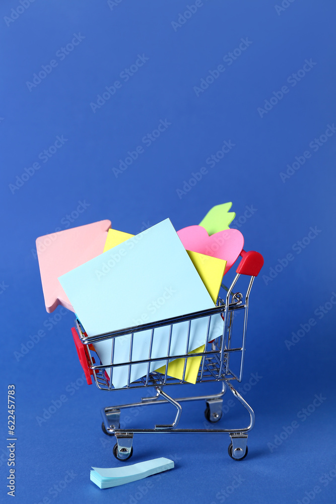 Shopping cart with different sticky notes on blue background