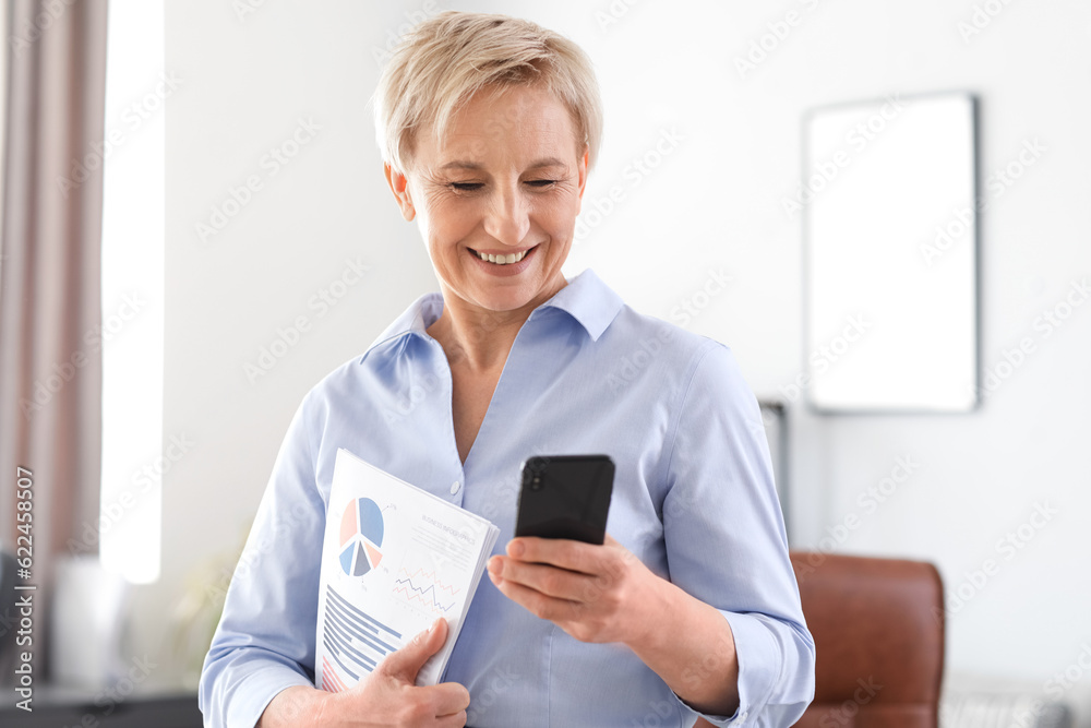 Mature businesswoman with documents and mobile phone in office