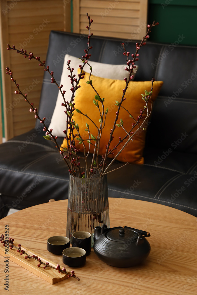 Vase with blooming tree branches and tea set on table in living room