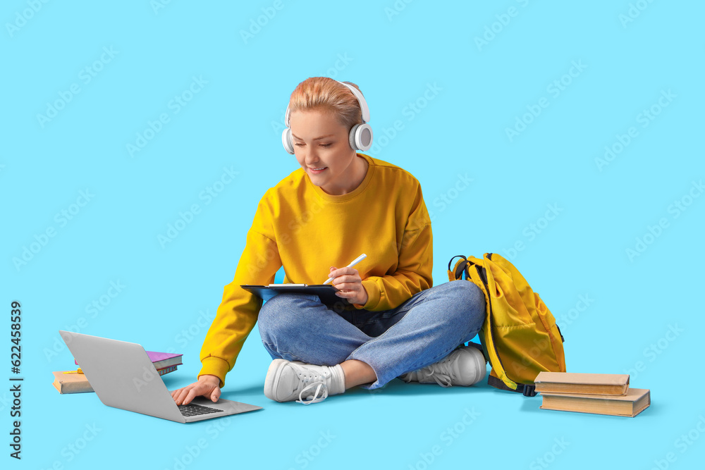 Female student in headphones using laptop on blue background