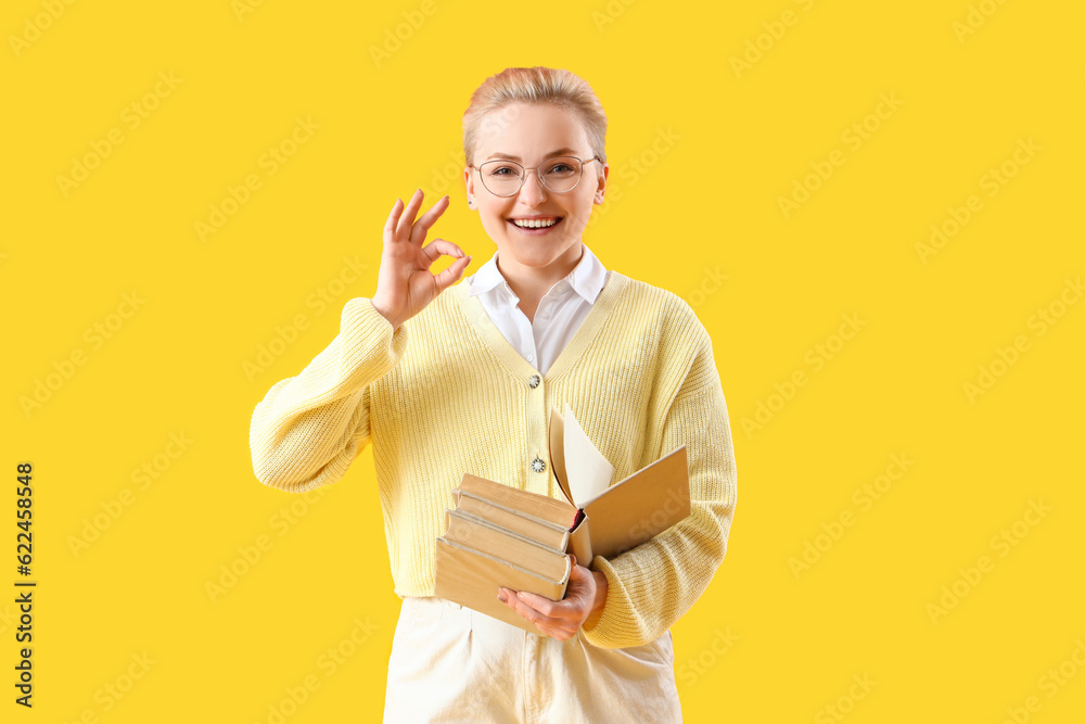 Female student with books showing OK on yellow background