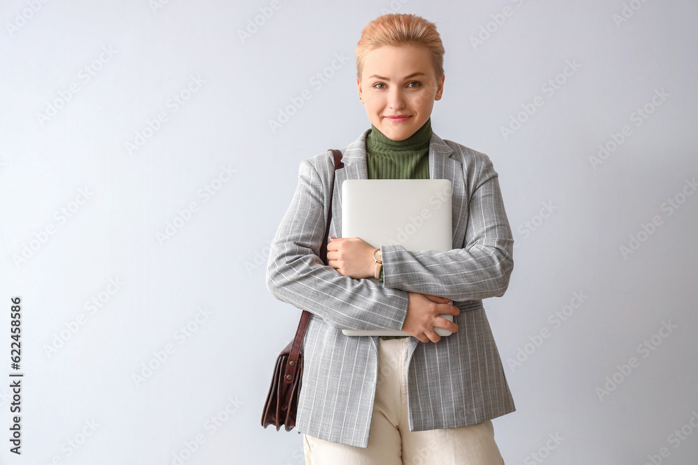 Female student with laptop on light background