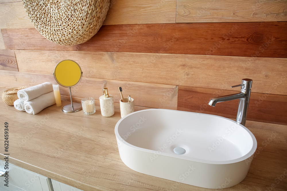 White sink with bath accessories on table near wooden wall