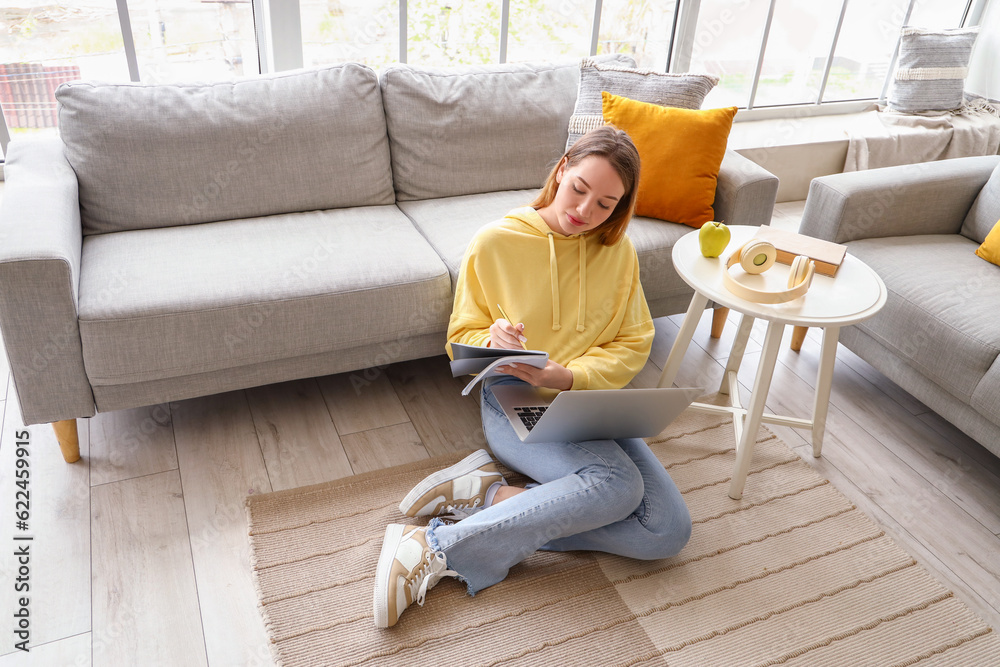 Female student studying with notebook and laptop at home