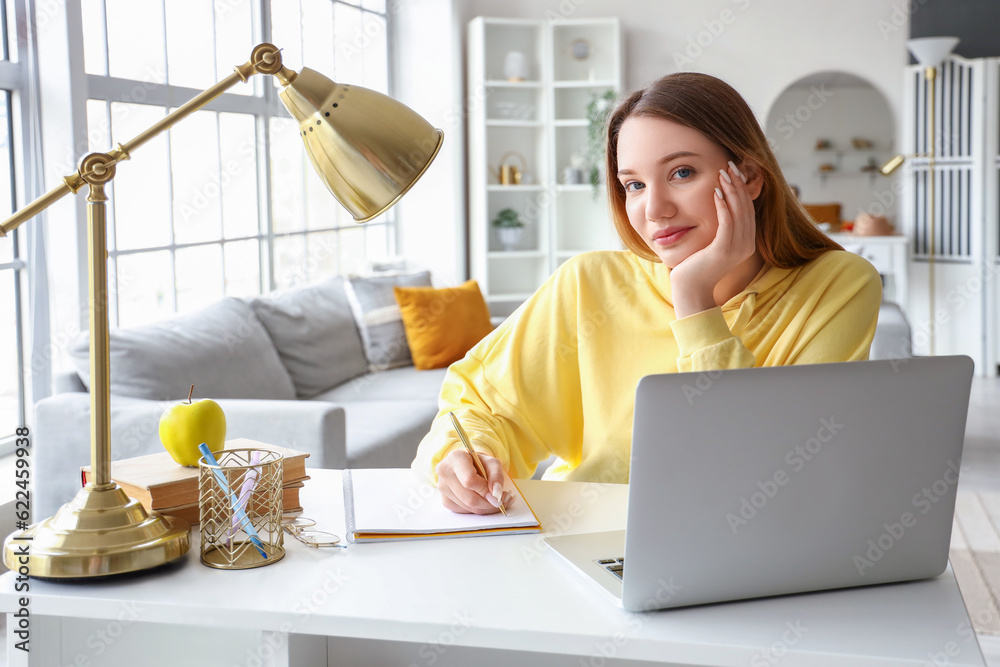 Female student writing in notebook at home